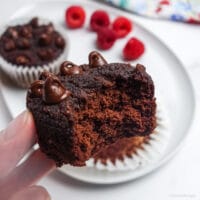 a vegan coconut flour chocolate cupcake held in a hand with a bite taken out of the cupcake