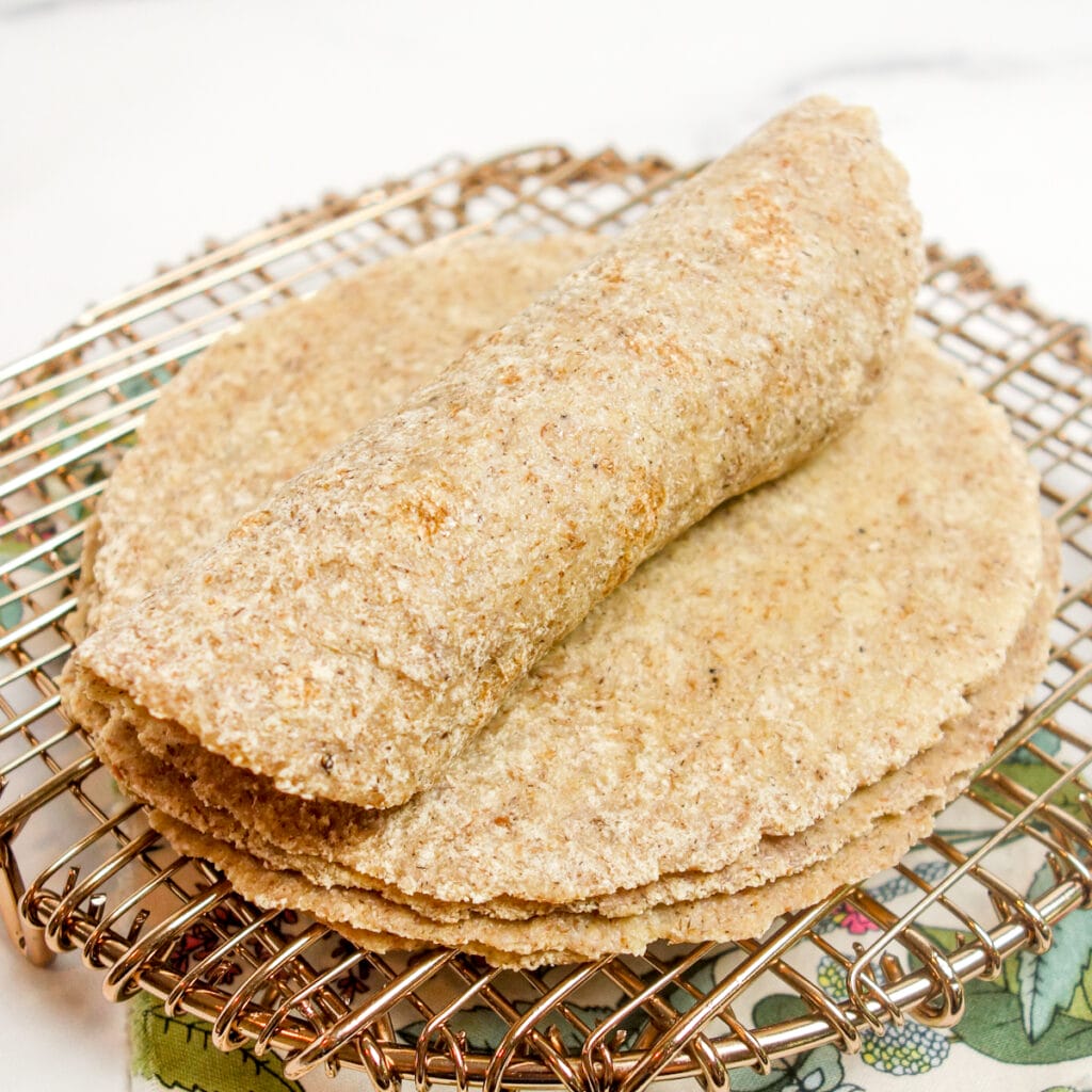 a rolled millet tortilla atop a stack of more millet tortilla