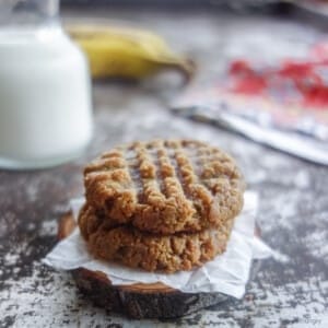 two peanut butter banana cookies with milk and bananas in the background