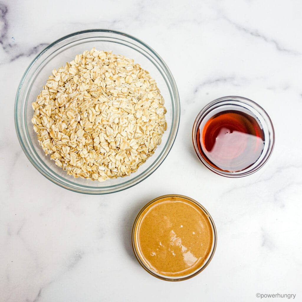 ingredients for 3 ingredient peanut butter granola , all in glass bowls on a marble surface