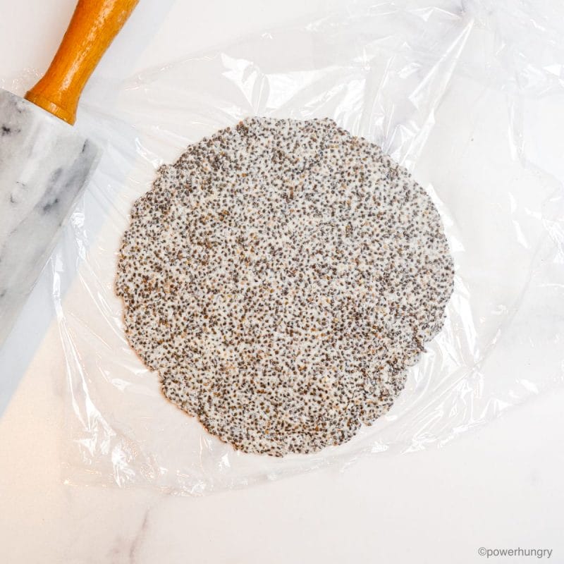a rolled out chia tortilla, in between two pieces of plastic wrap