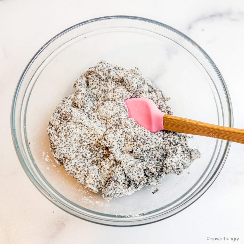a glass bowl with chia gel and coconut flour, getting stirred by a pink spatula