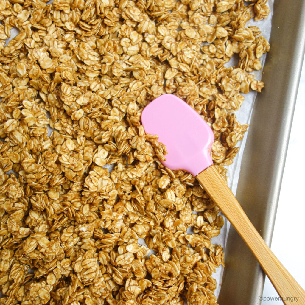 granola mixture spread on a parchment lined baking sheet