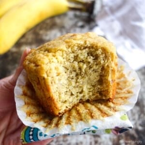 a banana chickpea muffin, held in a hand, with a bite taken out