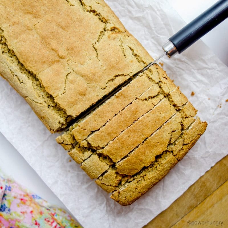 loaf of oat flour bread being cut into slices on a cutting board.