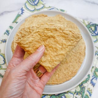 a folded oat fiber tortilla held in a woman's hand